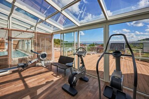 Un gimnasio con equipamiento de ejercicio, una banca y vistas al exterior.