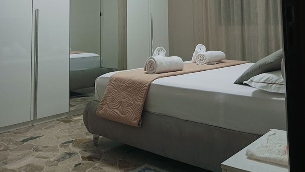 Quarto com cama, guarda-roupa, espelho e janela com cortinas.