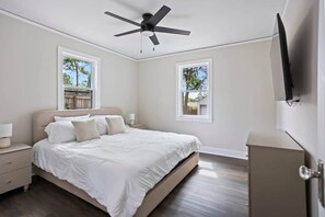 Ein Schlafzimmer mit einem Bett, Nachttischen, einem Deckenventilator, zwei Fenstern und einem Fernseher.