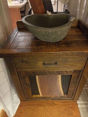 Un meuble en bois surmontĂ© dâun grand bol, dotĂ© dâun tiroir avec une poignĂ©e et dâun panneau en bois ornĂ© dâun motif gĂ©omĂ©trique.