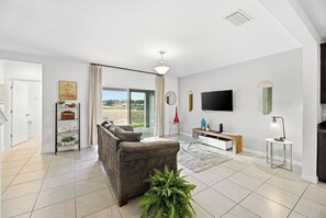 Ein modernes Wohnzimmer mit einer Couch, einem Fernseher und Blick ins Freie.