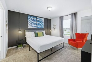 Ein modernes Schlafzimmer mit einem Bett, einem roten Sessel und einem großen abstrakten Gemälde an der Wand.