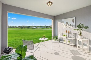 A modern room with a large window, a small round table, a chair, a white shelving unit with plants, and a painting of palm trees. - The Ultimate Family Getaway Near Disney (Davenport)