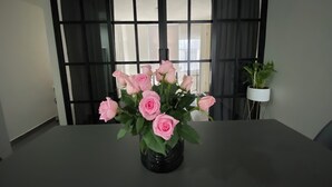 Ein Tisch mit einer Rosenvase in einem modernen Zimmer mit großem Fenster und einer Topfpflanze.
