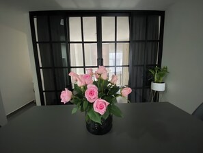 A table with a vase of pink roses in a modern room with a large window and a potted plant. - Beautiful apartment near Angel de la Independencia (Cuauhtémoc)
