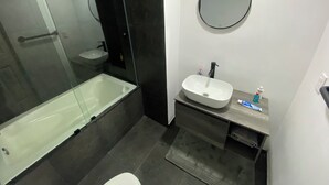 Ein modernes Badezimmer mit einer einteiligen Duschkabine, einem weißen Waschbecken und einem runden Spiegel.