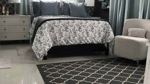 Ein Schlafzimmer mit einem Bett, einem Sessel, einem Nachttisch, einer Lampe und einem Teppich.