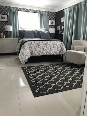 Ein Schlafzimmer mit einem Bett, einem Sessel, einem Nachttisch, einer Lampe und einem Teppich.