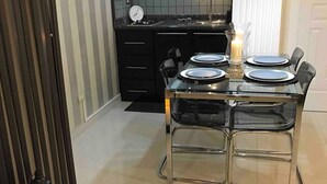 Eine moderne Küche mit Essbereich, ausgestattet mit einem Glastisch, Metallstühlen und einem schwarzen Schrank.