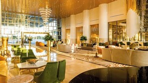 Eine großzügige Lobby mit hoher Decke, modernen Möbeln und einer imposanten Kristallleuchtre.'