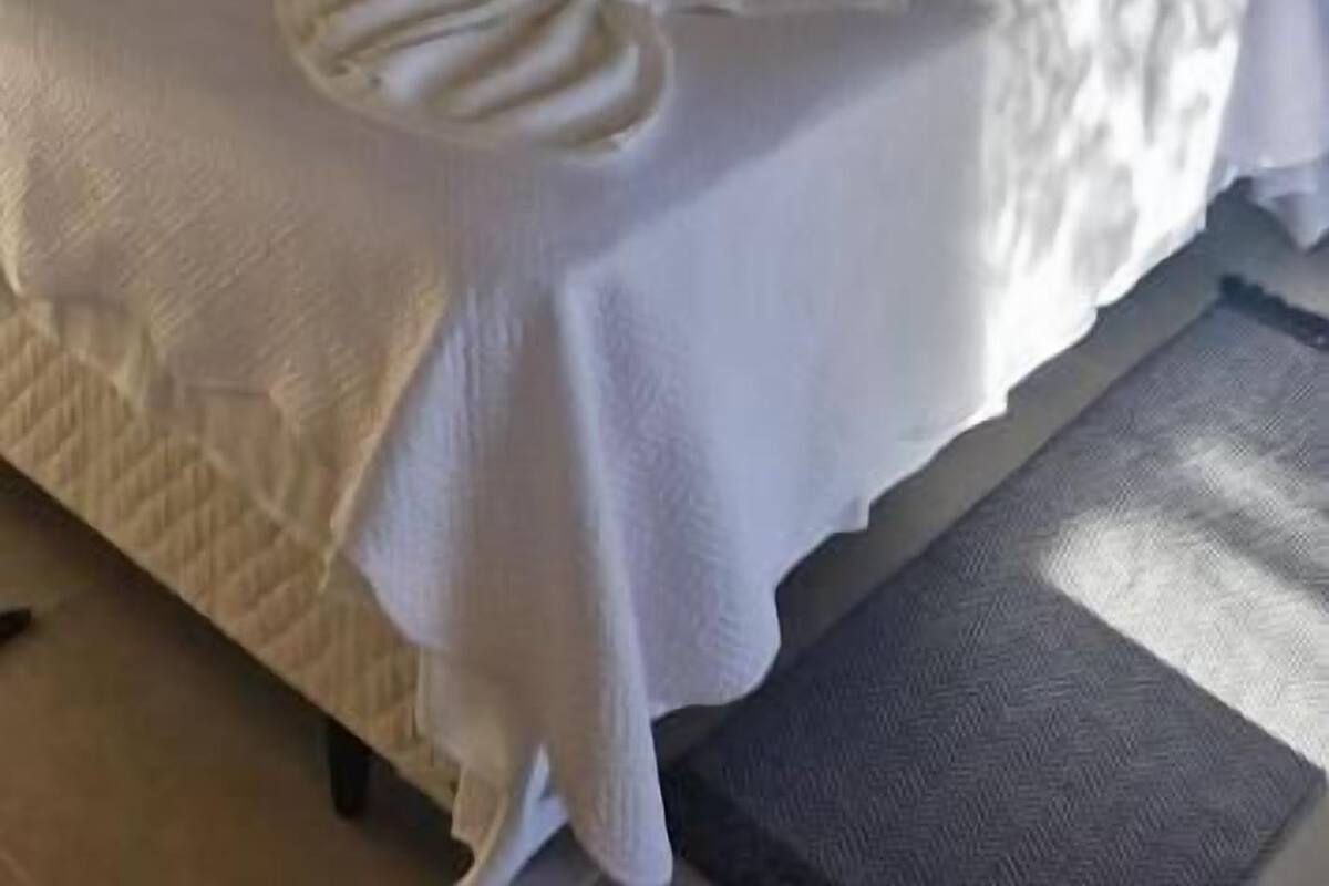 Una cama con cabecera de madera, una colcha blanca y un aire acondicionado de pared.