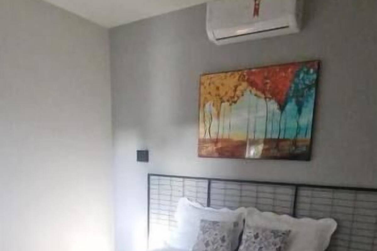 Una cama bien hecha con toallas, un cuadro en la pared y un equipo de aire acondicionado encima.