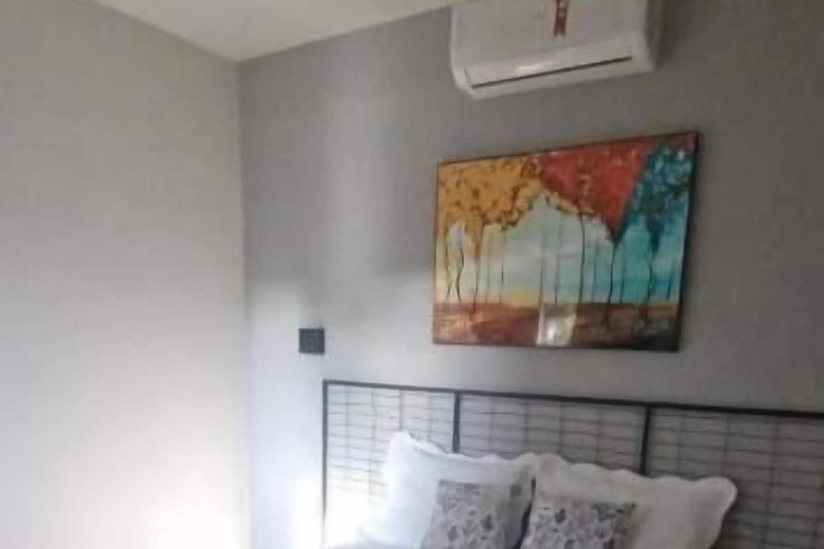 Ein ordentlich bezogenes Bett mit Handtüchern, ein Gemälde an der Wand und eine Klimaanlage darüber.