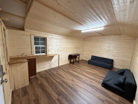 A room with wooden walls and flooring, a window, a sofa, and a small table.. Enchanting 1-bedroom off grid cabin surrounded by Wayne National Forest.