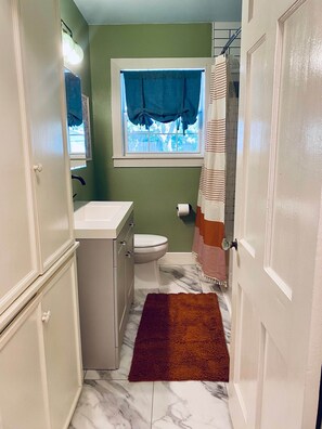 Un baño con inodoro, lavamanos y ventana con cortinas.