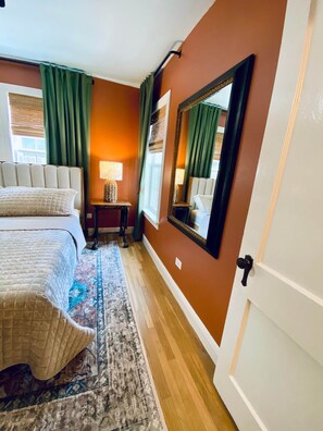 Una habitación de hotel con una cama grande, una mesita de noche con lámparas, un espejo y una alfombra estampada.