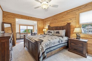 Ein Schlafzimmer mit Holzwandverkleidung, einem Bett, Nachttischen, einer Kommode und einem Deckenventilator.