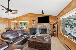 Ein Blockhaus-Interieur mit Ledersofa, Kamin aus Stein, Holzwänden und einem Fernseher.