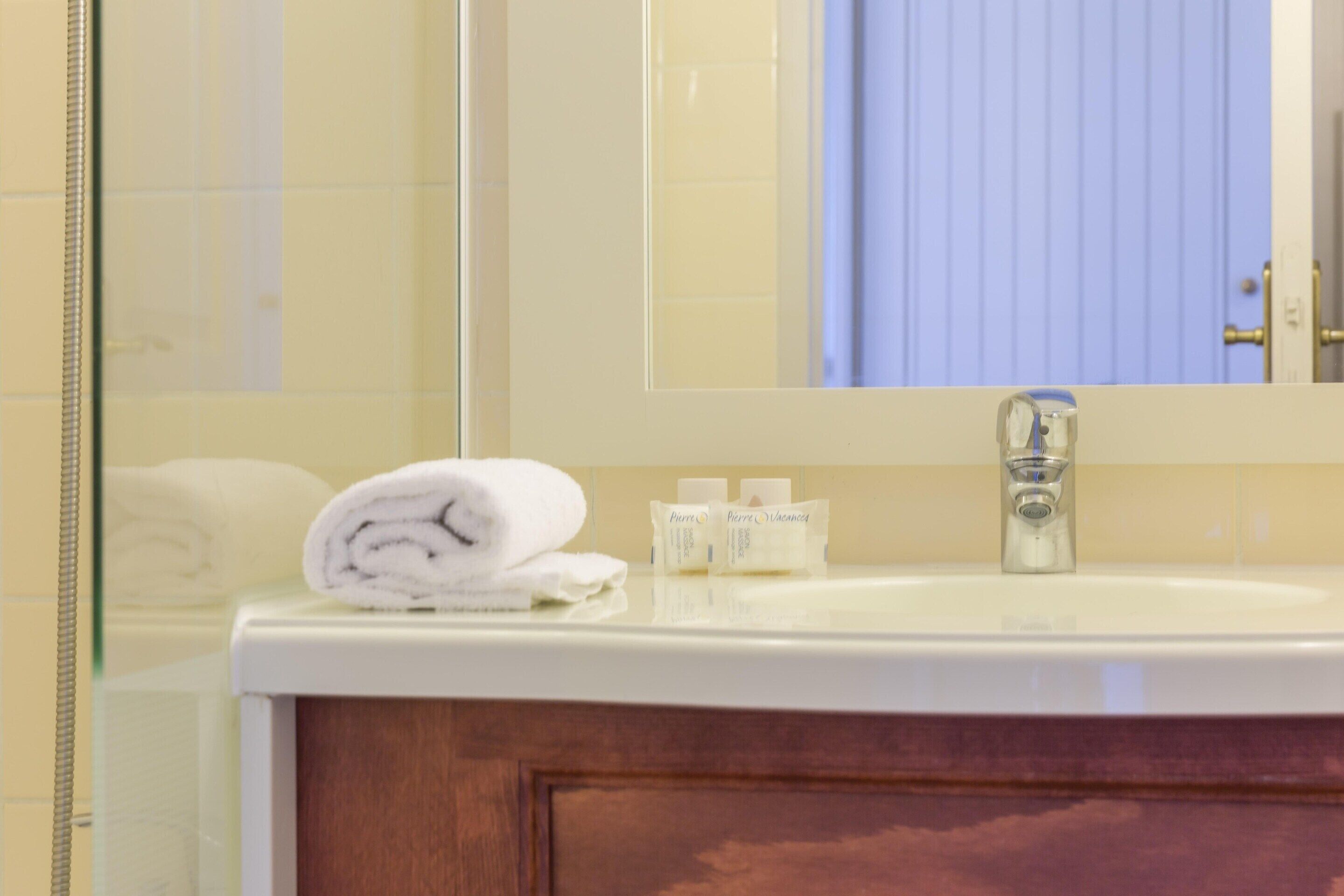 A bathroom with a white sink, a mirror, a towel, and toiletries.