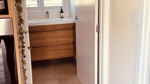 Ein Badezimmer mit einem Holzwaschtisch, einem Fenster mit Jalousien und einer Tür zu einem anderen Raum.