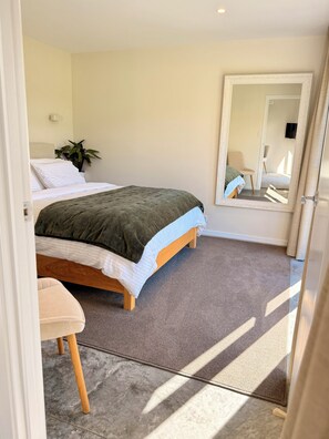 A bedroom with a bed, a chair, a potted plant, and a mirror.