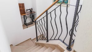 Eine Treppe mit einer Holzhandläufe und schwarzen Metallspindeln, die zu einem Raum mit einer Nähmaschine und einem gerahmten Gemälde führt.