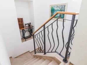 Eine Treppe mit einer Holzhandläufe und schwarzen Metallspindeln, die zu einem Raum mit einer Nähmaschine und einem gerahmten Gemälde führt.