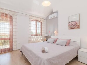 Ein Schlafzimmer mit Bett, Nachttisch, Klimaanlage und einem Vorhangfenster.