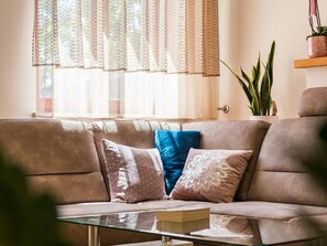Ein Wohnzimmer mit einer Couch, einem Glastisch und einer Topfpflanze.