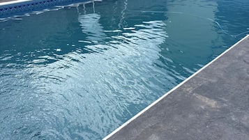 Piscina com escada, cercada por um muro de pedra e uma grade.