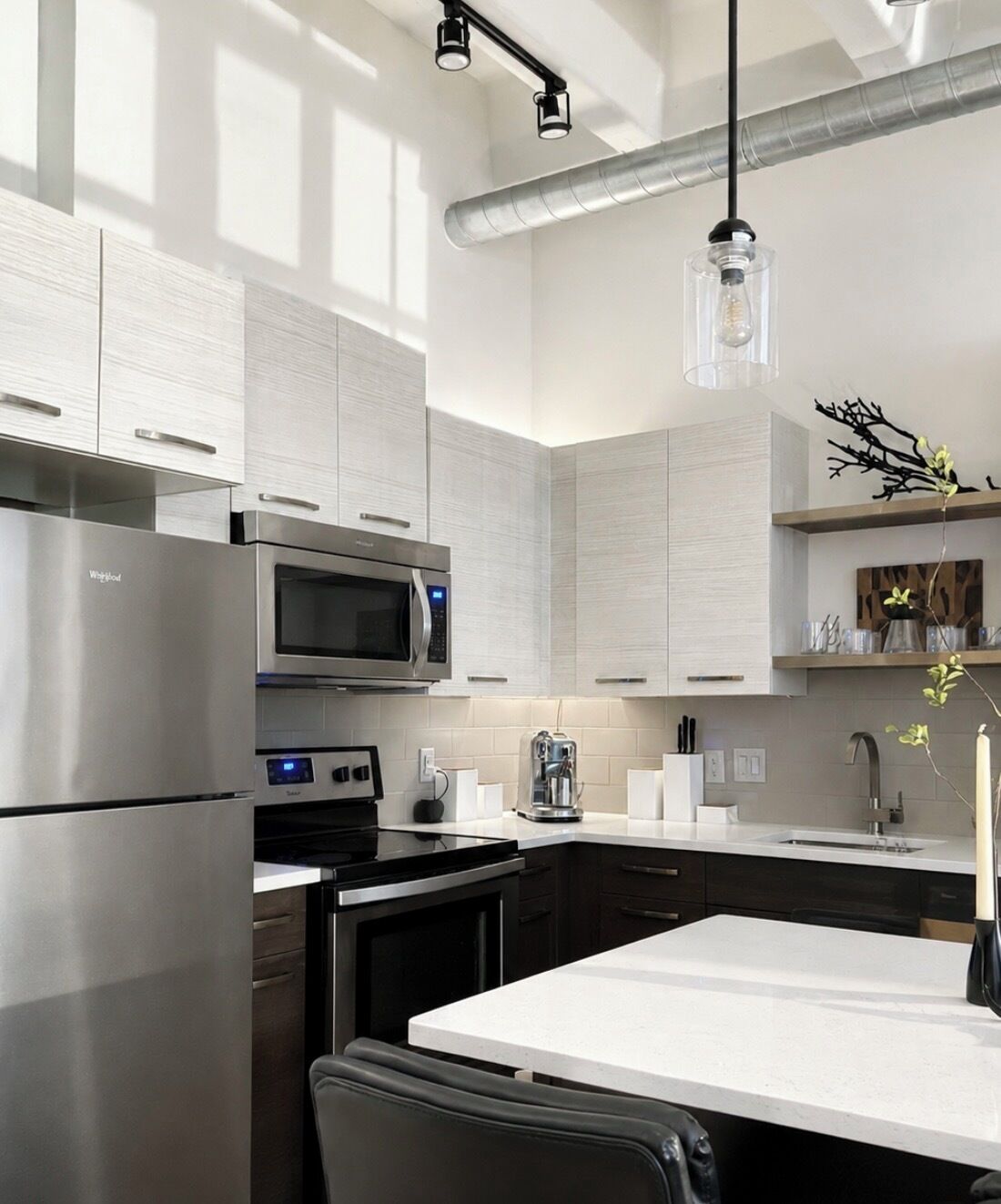 A modern kitchen with stainless steel appliances, a white countertop, and a hanging light fixture.