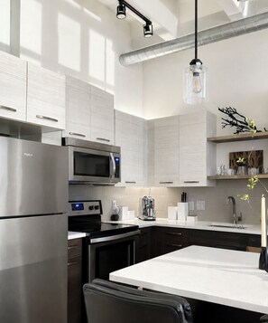 A modern kitchen with stainless steel appliances, a white countertop, and a hanging light fixture.