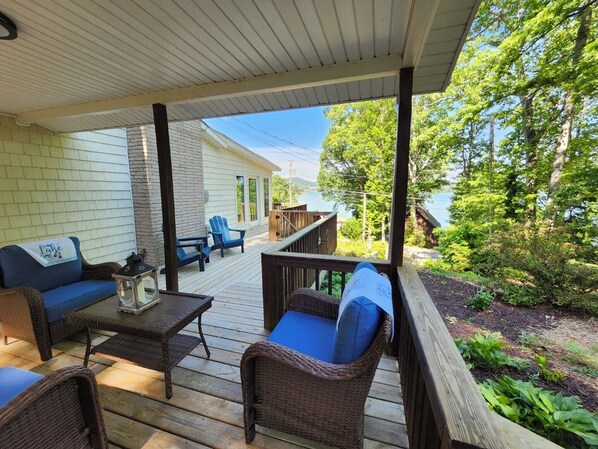 A covered outdoor deck with wicker furniture, a table, and a view of a lake and trees.