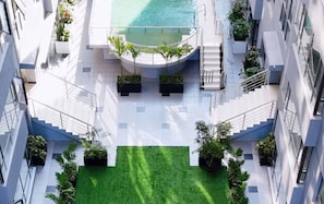 Ein modernes Gebäude mit einem zentralen Innenhof, einem Pool und mehreren Balkonen mit Pflanzen.