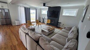 A modern living room with a sofa, chairs, a fireplace, and a kitchen area.