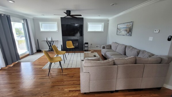 A spacious living room with a large sofa, two yellow chairs, a fireplace, and a ceiling fan.