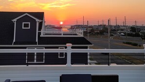 A balcony with two dark blue lounge chairs, a building with a white railing, and a sunset over a residential area. - Near Everything, Seaside Hgts/Ortley Beach (Seaside Heights)