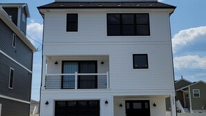 A two-story residential building with a garage, a balcony on the upper floor, and a clear sky with clouds. - Near Everything, Seaside Hgts/Ortley Beach (Seaside Heights)