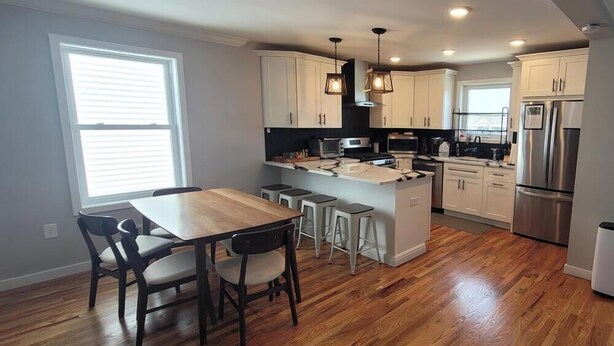 A modern kitchen with white cabinets, stainless steel appliances, and a wooden dining table with chairs. - Near Everything, Seaside Hgts/Ortley Beach (Seaside Heights)