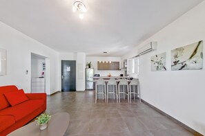A modern living room with a red sofa, a kitchen with bar stools, and a dining area. - Hideaway With Private Sun Deck (Lecci)