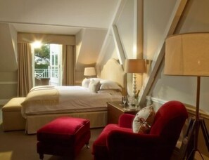A hotel room with a bed, a red armchair, a nightstand, and a lamp. - Chewton Glen Hotel and Spa (New Milton)
