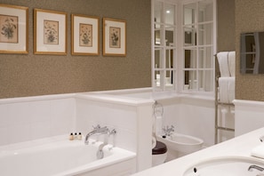 A bathroom with a bathtub, toilet, sink, and a window with a view. There are framed botanical prints on the wall. - Chewton Glen Hotel and Spa (New Milton)