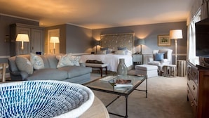 A well-lit, modern bedroom with a large bed, a sitting area with a sofa and armchairs, a coffee table, and a television. - Chewton Glen Hotel and Spa (New Milton)