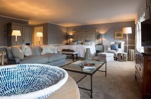 A well-lit, modern bedroom with a large bed, a sitting area with a sofa and armchairs, a coffee table, and a television. - Chewton Glen Hotel and Spa (New Milton)