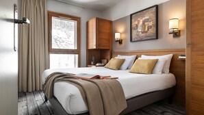 Ein Hotelzimmer mit einem großen Bett, einem Holz-Kopfteil, einem Fenster mit Vorhängen, einer Wandleuchte und einem Gemälde.