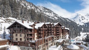 Ein mehrstöckiges Hotel mit Balkonen, im Hintergrund eine Skipiste und ein Poolbereich.