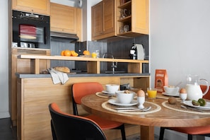 A modern kitchen with wooden cabinets, a built-in oven, and a breakfast setup with orange juice, eggs, and cereal. - Aesthetic 4-person Alpine Sanctuary (Araches-la-Frasse)