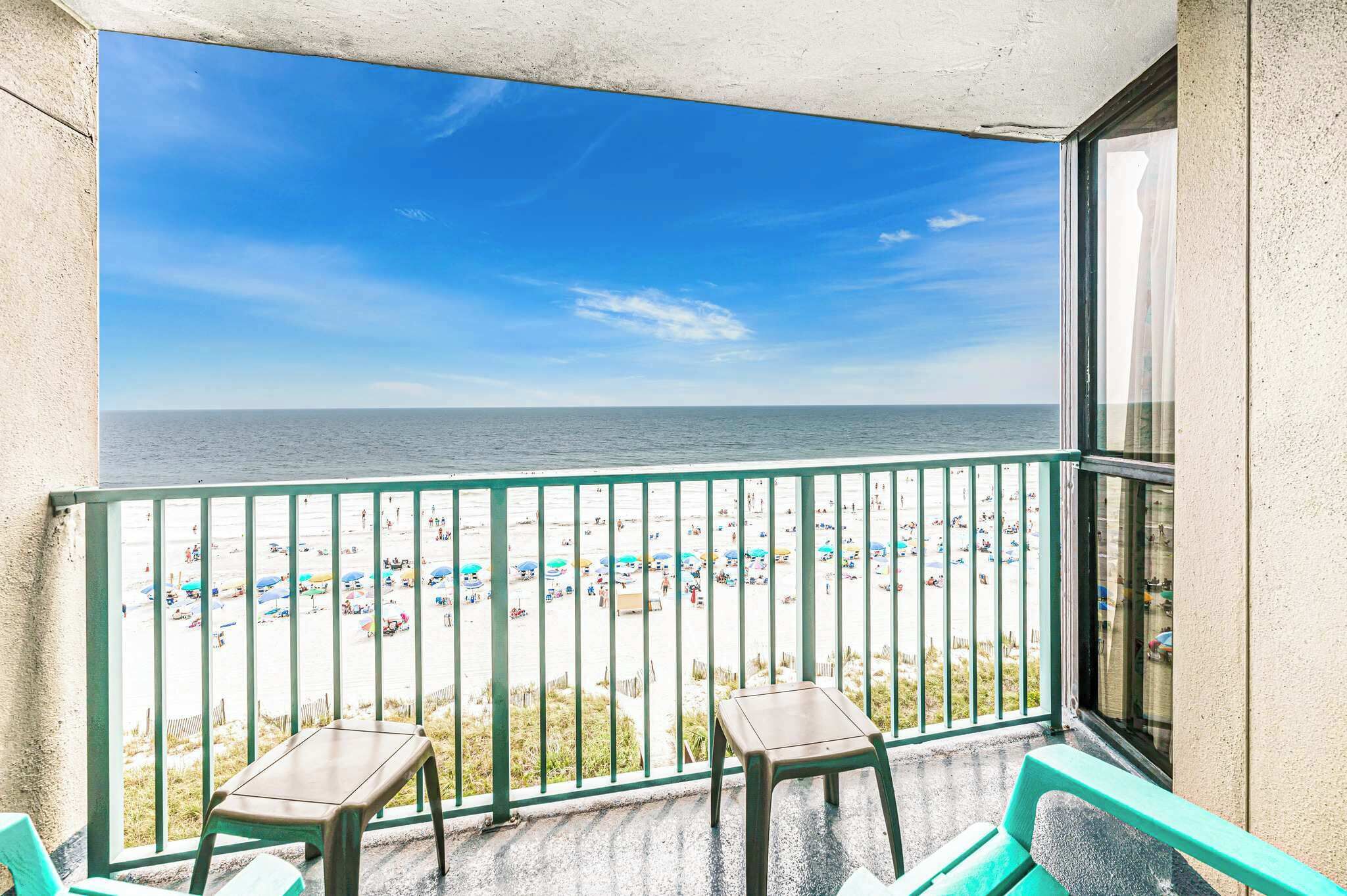A balcony with a view of a beach, two chairs, and a table.