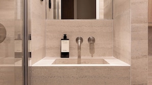 A modern bathroom with a glass shower enclosure, a sink with a soap dispenser, and a wooden cabinet below. - Cozy Studio A/C 1P - Arc de Triomphe (Paris)