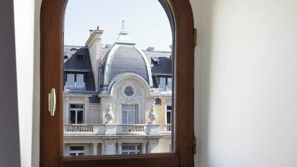 A room with a wooden-framed window overlooking a building with classical architecture. - Cozy Studio A/C 1P - Arc de Triomphe (Paris)